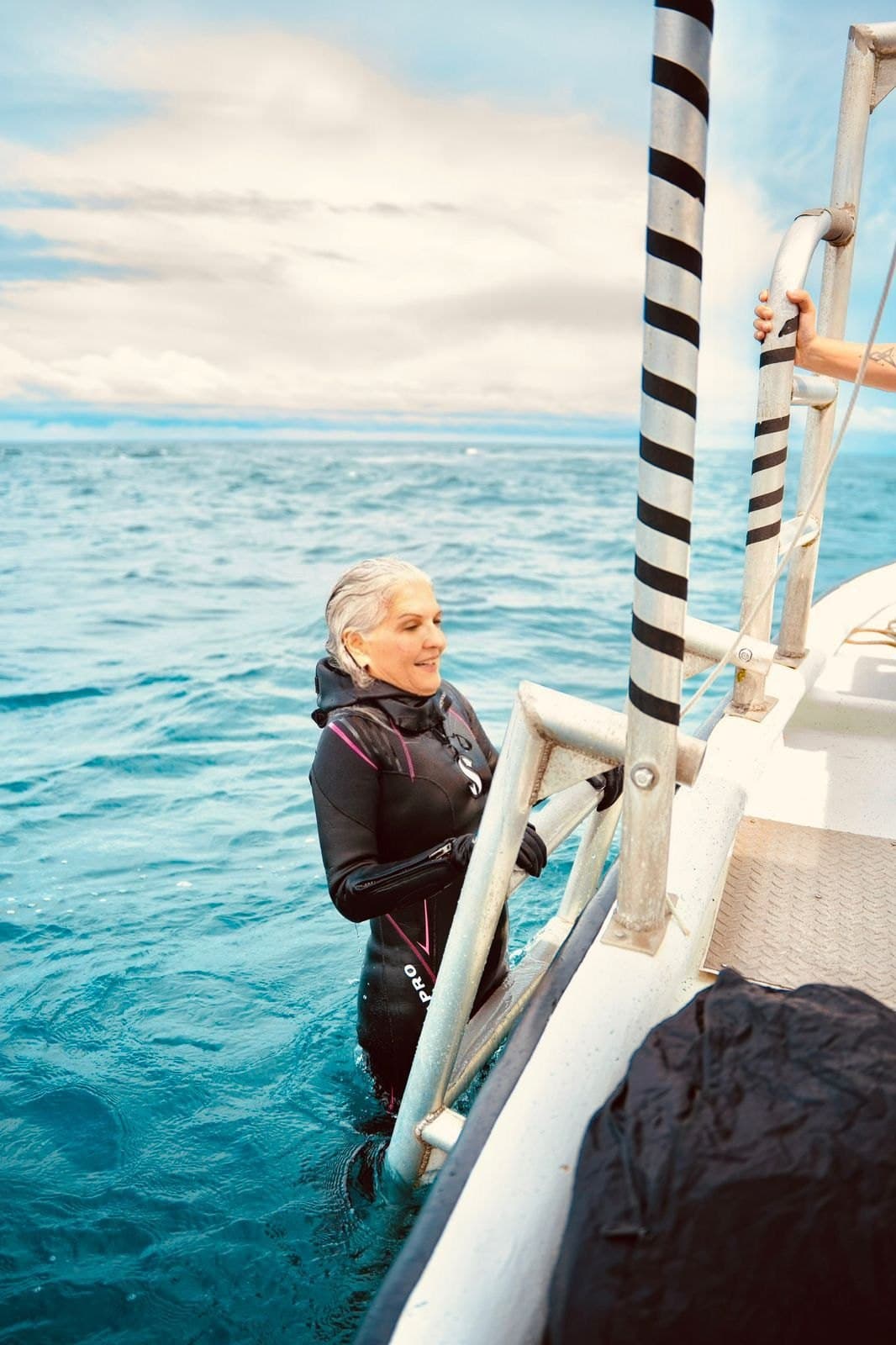Ofelia Mercedes Méndez con traje de buceo, saliendo del mar hacia la escalerilla de un bote